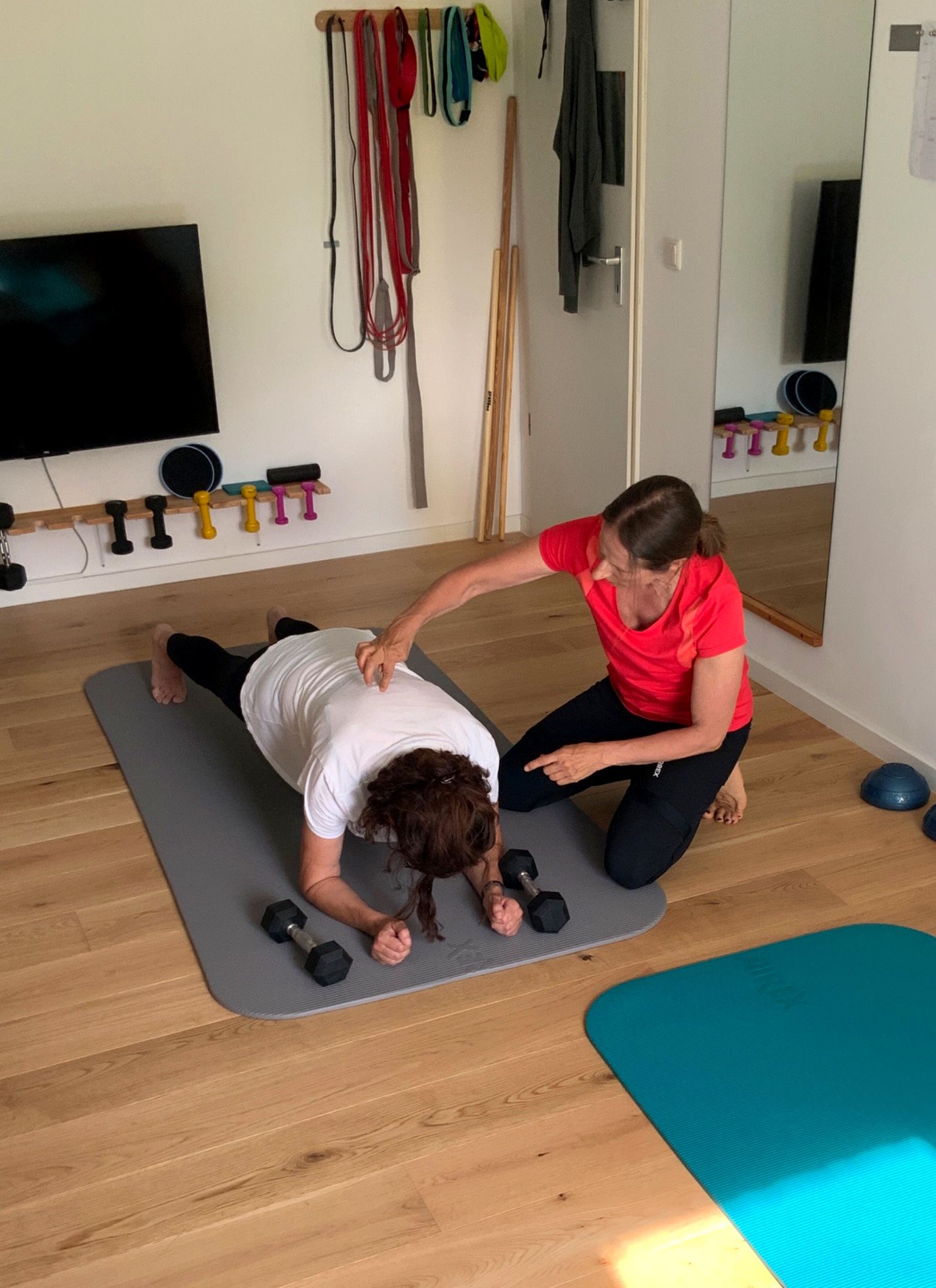 Personal Training in Leichlingen und Langenfeld: Dr. Annette Schimmel korrigiert eine Kundin bei der Plank-Übung mit Kurzhanteln im Home-Studio