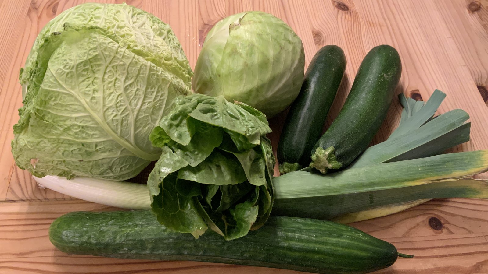 Grünes Gemüse auf einem Holztisch: Wirsing, Weißkohl, Romanasalat, Zucchini, Lauch und Gurke, Ernährung für starke Knochen bei Osteoporose